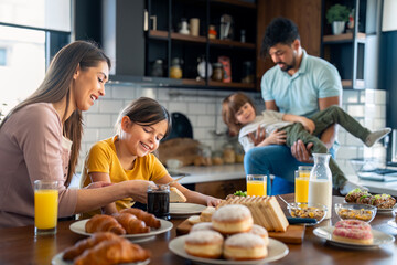 Mother and father at breakfast with son and daughter in the kitchen at home. Playful family having...