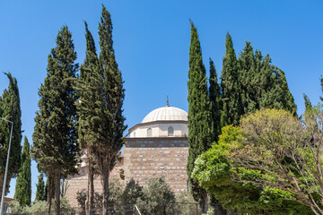 A beautiful view of the Karacabey imaret mosque's dome and minaret from the outside, with a blue sky and trees in the background.