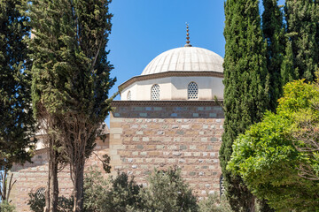 A beautiful view of the Karacabey imaret mosque's dome and minaret from the outside, with a blue sky and trees in the background.