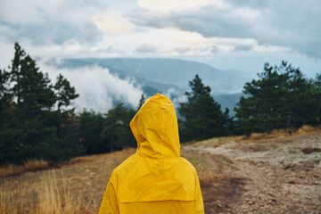 Person in a yellow raincoat enjoying the breathtaking view of the majestic mountains on a tranquil...