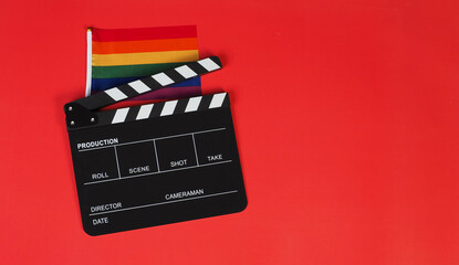 Clapper board and rainbow pride flag on red background.