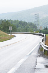 mountain road in Norway with metal barrier barriers with a sharp bend. mountains can be seen in the distance.