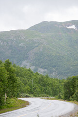 Winding mountain country road in Norway overlooking large fjords on a foggy, rainy summer day.