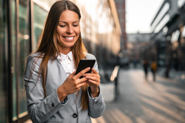 Smiling businesswoman using a mobile phone against a city background.