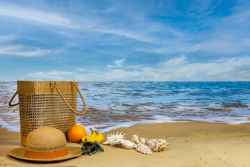 Seashells, basket, fruits, hats and sunglasses on a sandy beach against the backdrop of the sea and...
