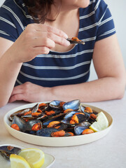 woman with a mussel in its shell in her hand ready to eat in front of a large platter with cooked mussels and lemon.