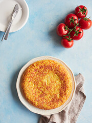 typical homemade Spanish potato omelette with fresh red tomatoes on a blue background