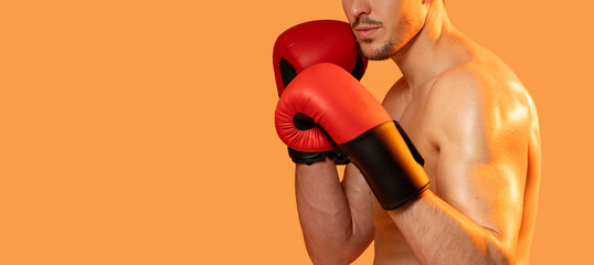 A man stands wearing boxing gloves against a vibrant orange background. He appears ready for a...
