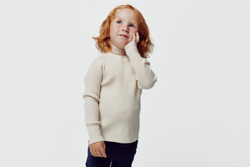 Curious little girl with red hair standing in front of white background with hands on face...