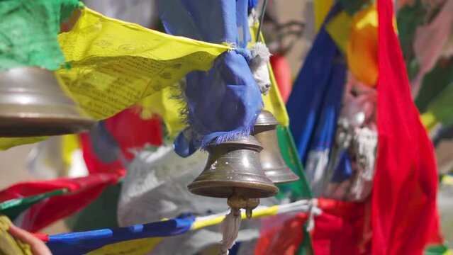 Closeup shot of hand ringing temple bell surrounded by buddhist prayer flags at Kunzum Mata temple on the top of the Kunzum Pass on the way to Spiti Valley in Himachal Pradesh, India. Hand rings bell.
