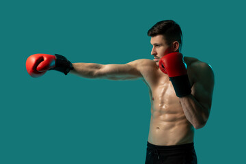 A muscular man is practicing boxing by throwing punches indoors against a solid blue background. He...