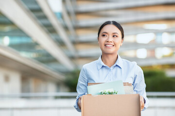 Excited Asian businesswoman is standing while holding a cardboard box. She appears focused and...
