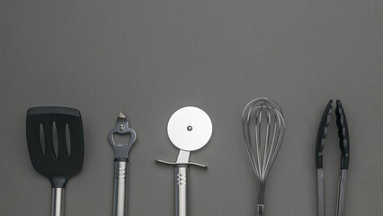 Various Kitchen Utensils on Gray Background - Spatula, Peeler, Pizza Cutter, Whisk, Tongs