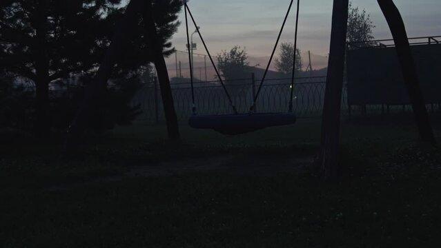 Empty swing on children's playground swinging at foggy night. Horrible poltergeist and ghost concept	