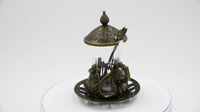 Close-up side view of empty armudu (armuda, bogmaly) - traditional metal and glass tea or coffee cup with small spoon from Turkey or Azerbaijan. Souvenir from travel turning on gray background.