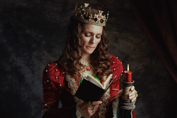 stressed medieval queen in red dress with book and candle