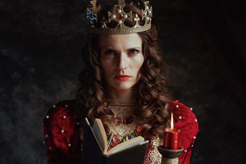 medieval queen in red dress with book, candle and crown