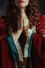 Closeup on medieval queen in red dress with rosary praying