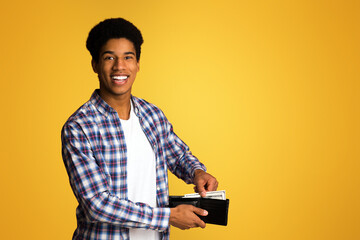 Money saving. African-american guy putting banknotes into wallet, orange background