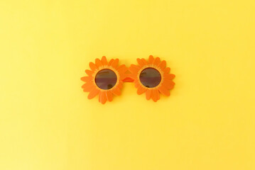 A pair of orange floral funny sunglasses on yellow background with copy space