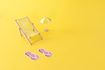 A small beach chair, umbrella and slippers on a yellow background, summer vacation concept