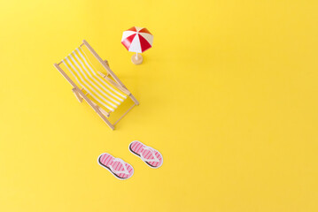 top view of A small beach chair, umbrella and slippers on a yellow background, summer vacation...