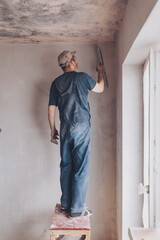 Male builder in work overalls plastering a wall using a construction trowel. Plasterer home...