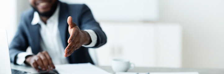 Cropped of african american businessman outstretching his hand towards camera, sitting at desk at modern office, greeting business partner, panorama with copy space
