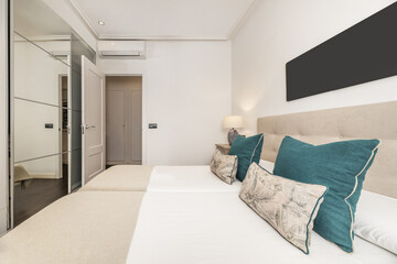 Bedroom with two single beds joined by a fabric-upholstered headboard, lamps with two shades and a large wardrobe with sliding mirror doors