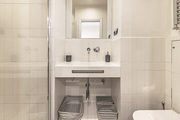 Front image of a small white tiled bathroom with a small frameless mirror and glass shower cubicle