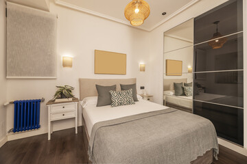 bedroom with double bed with fabric upholstered headboard, illuminated wall lights, cushions of various colors and built-in wardrobe with sliding glass doors and mirror
