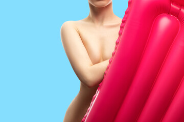 A young slender girl holds a pink inflatable mattress on a blue background.
