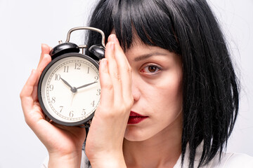 A businesswoman holding an alarm clock and covering her face