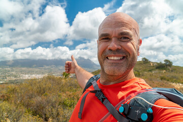 Smiling hiker takes a selfie in the top of a mountain.