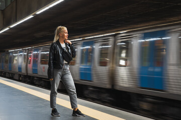 A blonde girl of European appearance is standing in the subway and a train passes by.