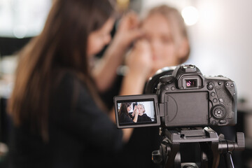 Woman make makeup for attractive blond hair woman in studio. Selective focus of digital camera with makeup artist applying cosmetics for beautiful model