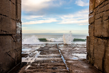 View of the sea at dawn, framed by two walls, breaking against a breakwater.