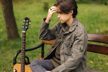 Portrait of handsome teenage boy playing guitar outdoor. Boy using classic guitar. Male alone...