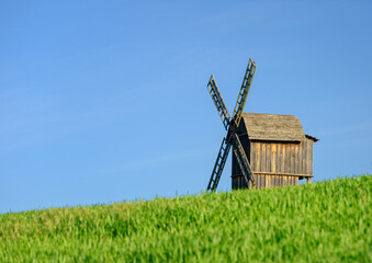 telephoto view to old wooden windmill in green field under blue sky with copy space