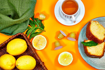 Glass cup with lemon, mint tisane with a bouquet of gypsophila flowers and pound cake on yellow background