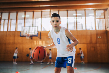 Basketball kid dribbling a ball on training and looking at camera.
