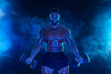 Sporty fit man athlete with dumbbells make fitness exercises on blue neon background. Download cover for music collection for fitness classes. Sports recreation.