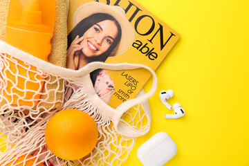 String bag with fresh oranges, fashion magazine and beach accessories on yellow background, flat...