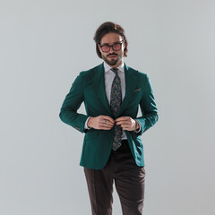 confident elegant man with sunglasses buttoning green suit and walking