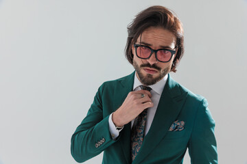 sexy unshaved businessman with sunglasses fixing suit tie