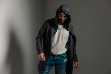 confident casual man with glasses in long hoodie looking down and posing
