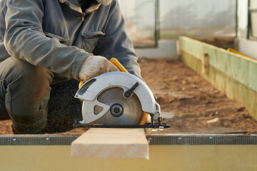 A man cuts a board with a circular saw to reinforce a bed in a greenhouse.