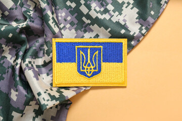 Military badge of Ukrainian army with trident and camouflaged uniform on beige background