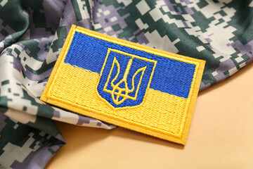 Military badge of Ukrainian army with trident and camouflaged uniform on beige background