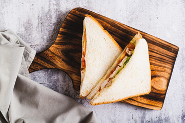 Close up of appetizing sandwich with chicken breast, tomatoes, lettuce and sauce on a board top view